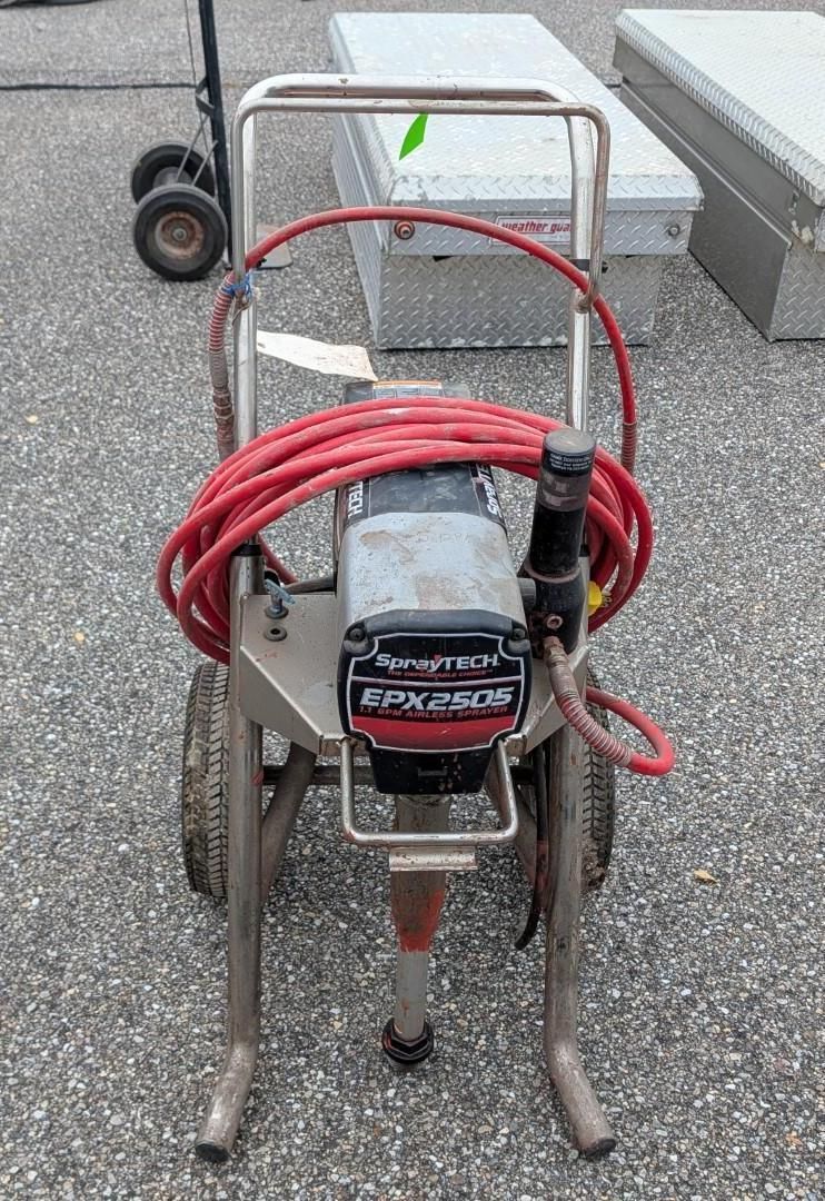 Red hose reel pressure washer on a metal cart sitting on gravel outdoors.