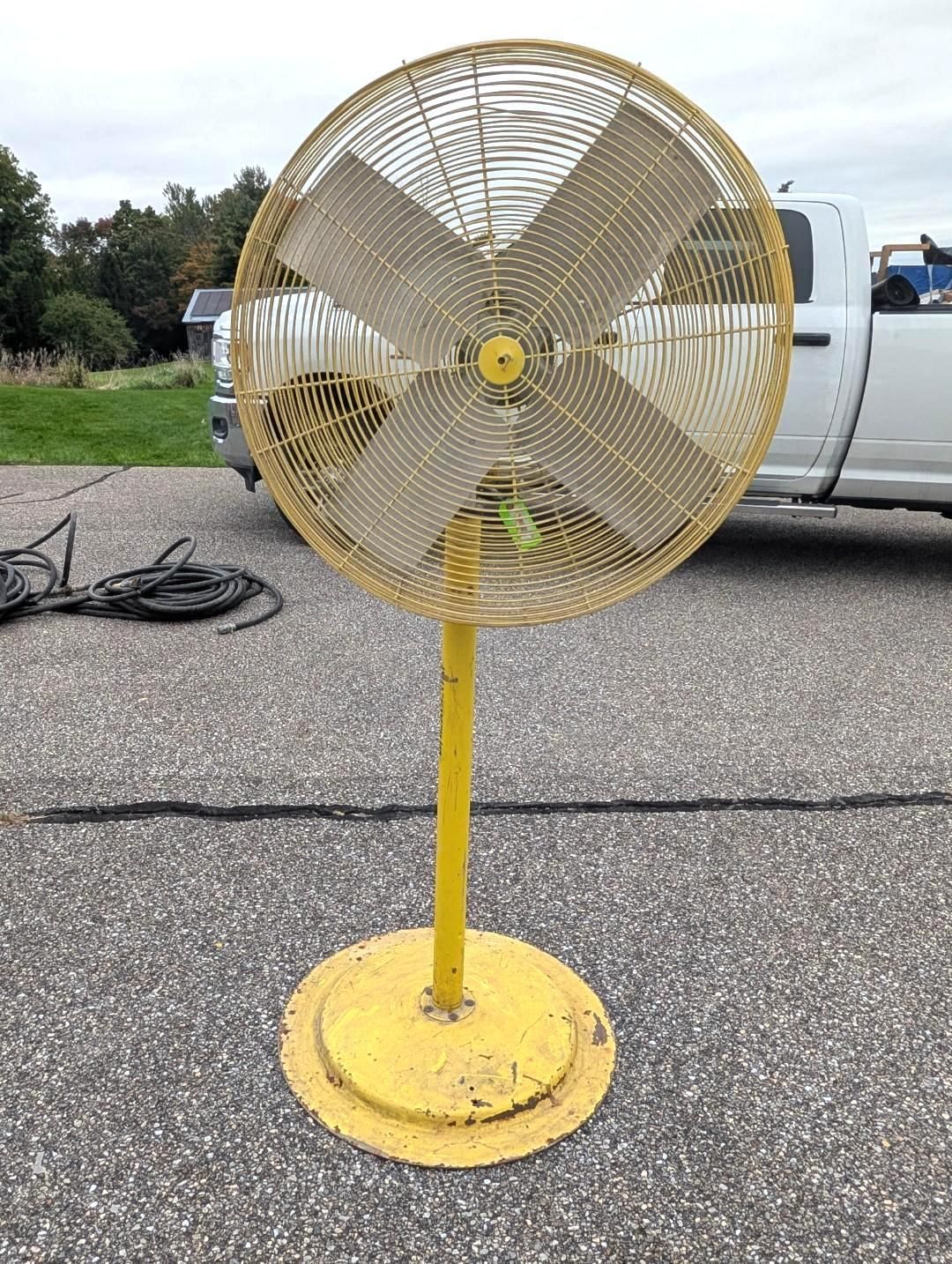Yellow industrial floor fan on a stand outdoors in a parking lot near a white truck.