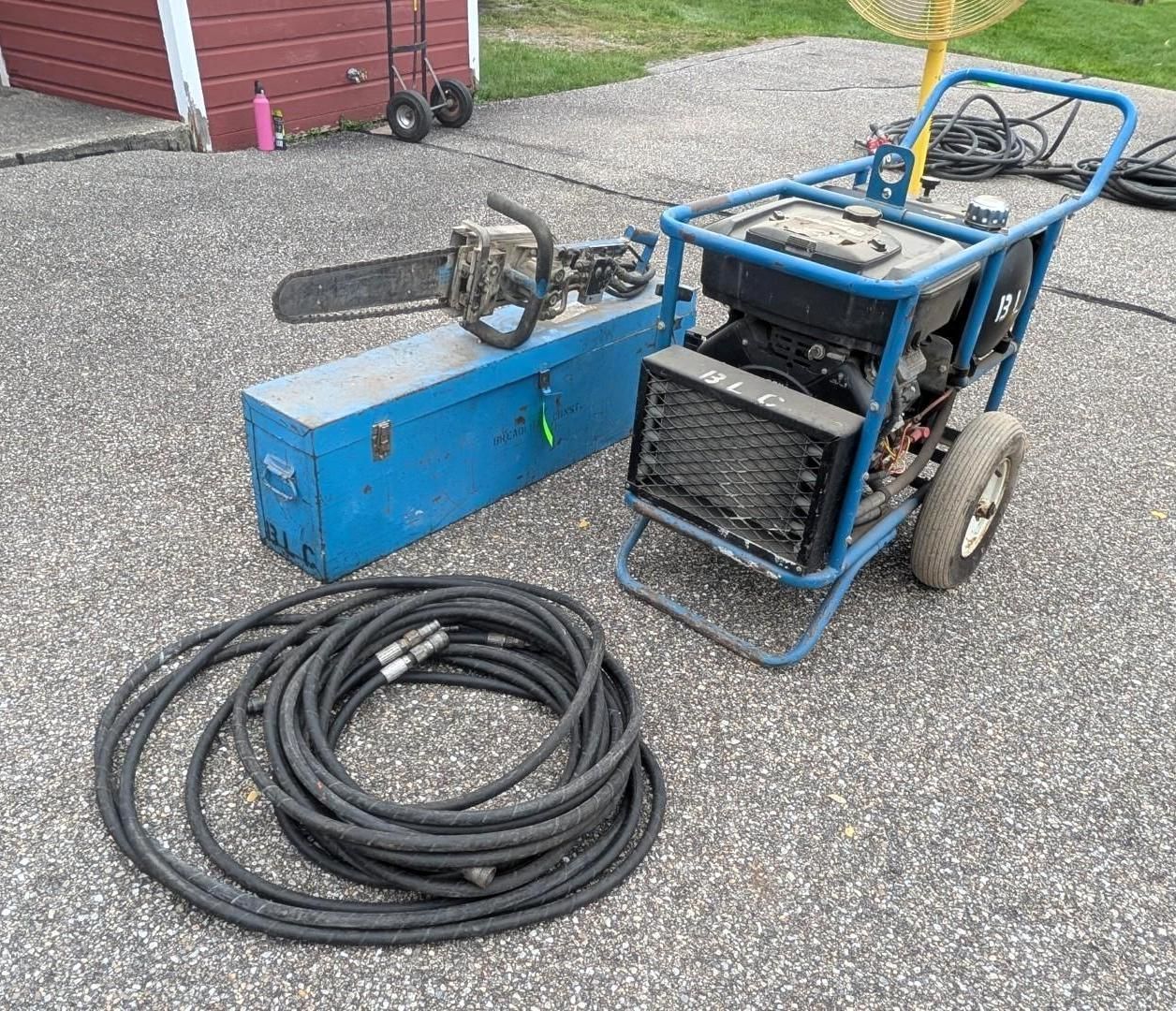 Blue pressure washer on gravel with coiled black hose and blue box near a red shed