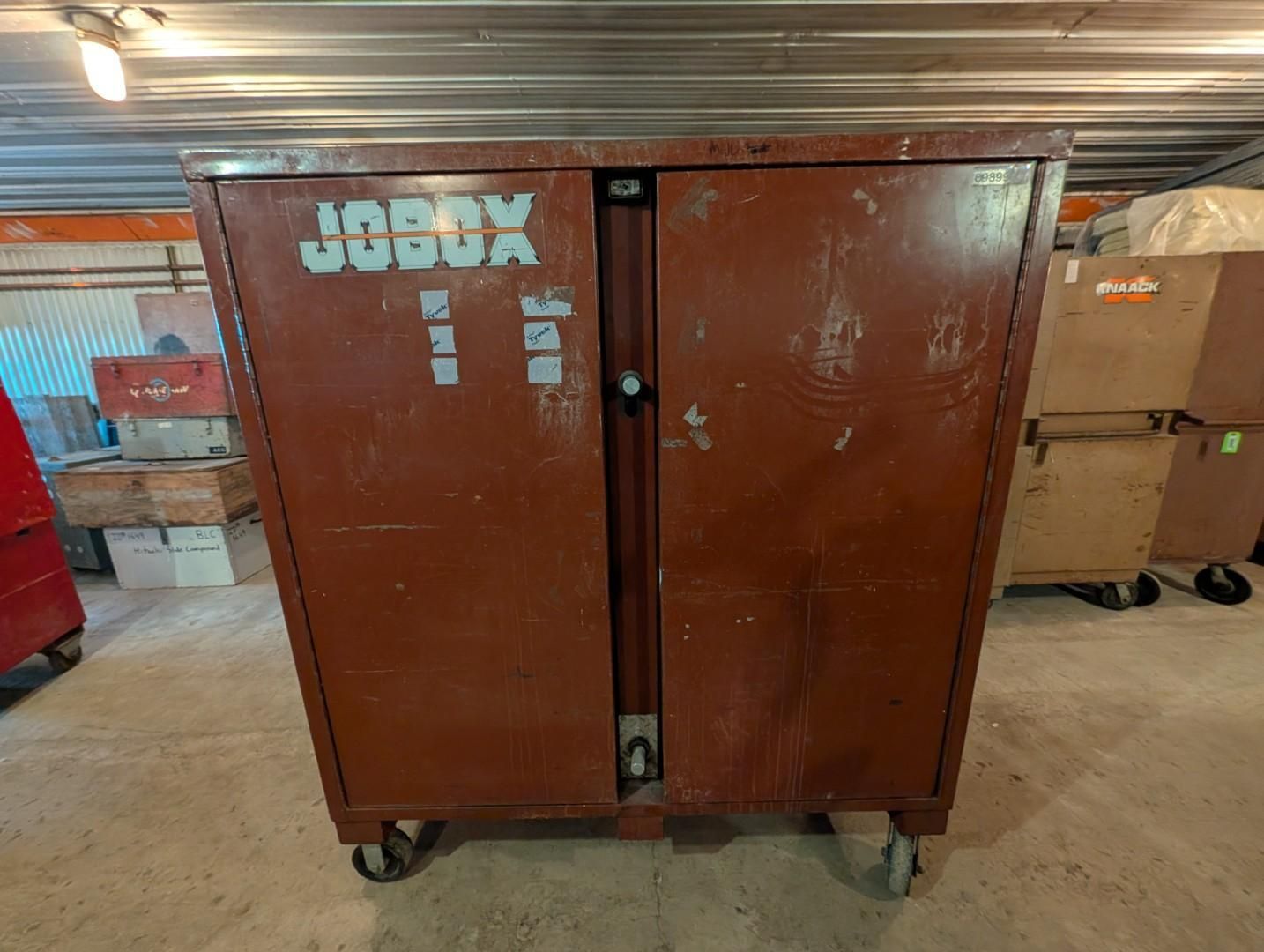 Brown metal storage cabinet on casters in a warehouse, with boxes and pallets in the background