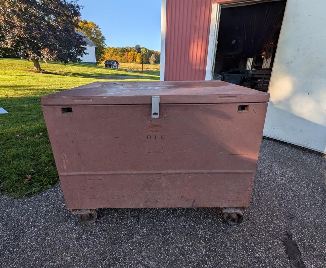Large brown wheeled storage chest beside an open garage on a driveway, with a grassy yard in the background