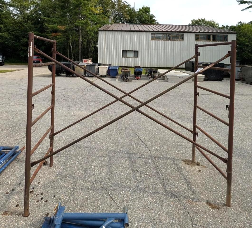 metal scaffolding frame on a gravel lot in front of a white industrial building