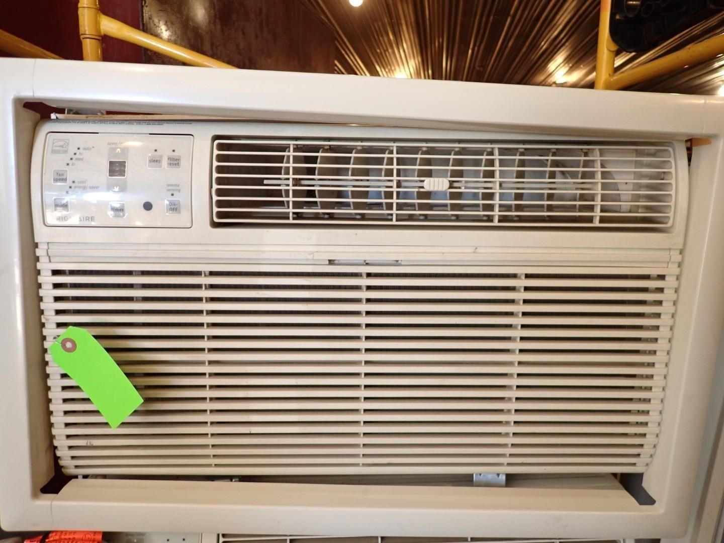 Window air conditioner in a white frame, with a green price tag attached to the left side.