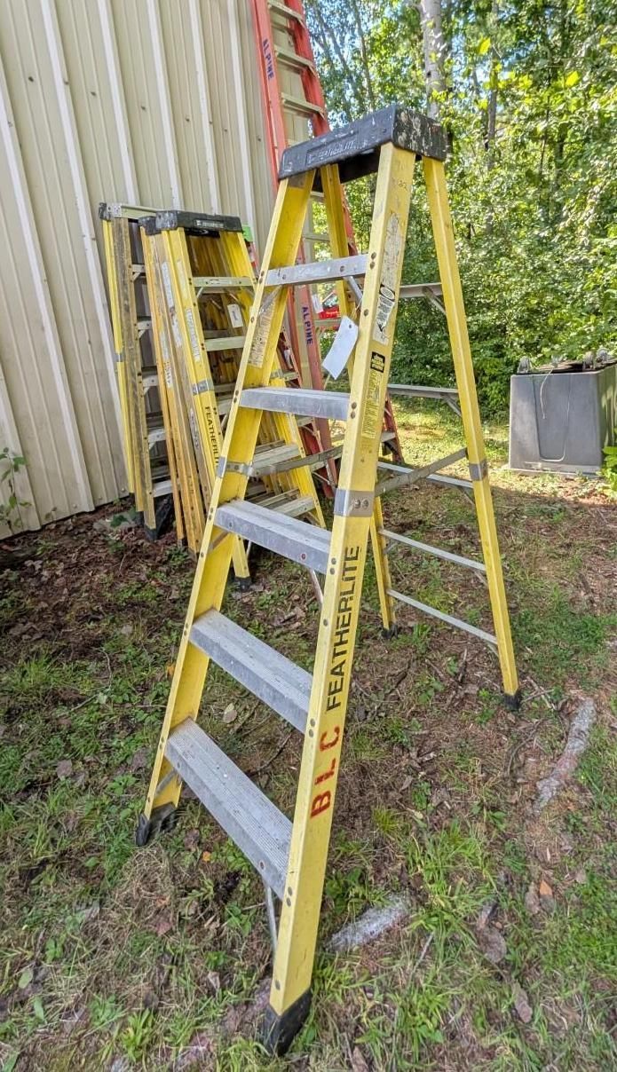 Yellow step ladder leaning against a corrugated metal wall outdoors on grass