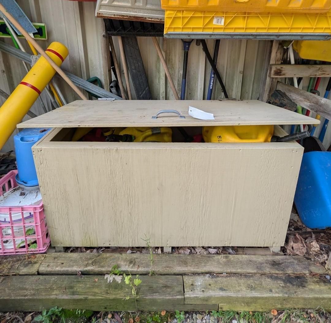 outdoor storage area with a beige cabinet, blue bins, yellow pipes, and a pink basket