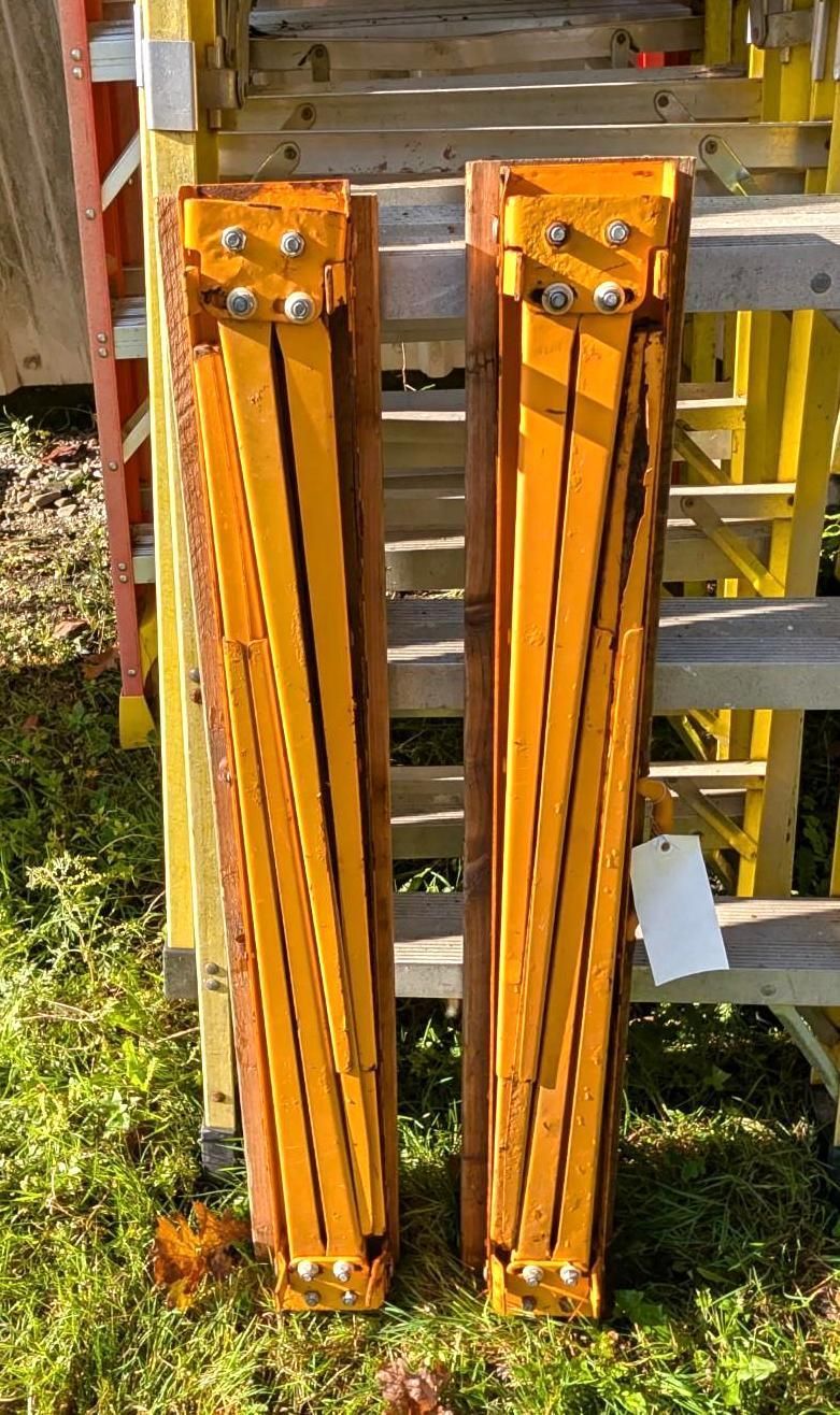 Two orange folding ladder sections leaning against a wooden structure outdoors.