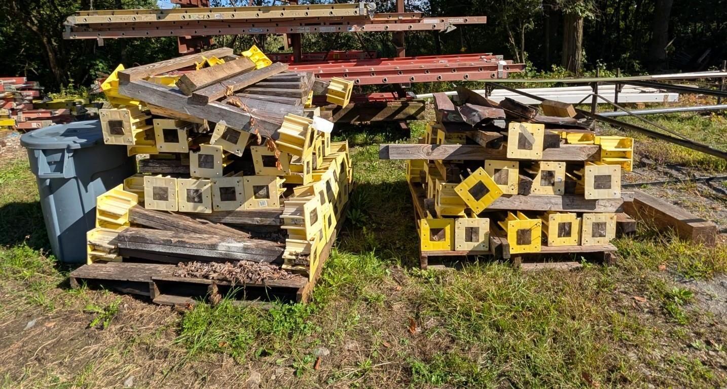 Stacks of yellow-and-black wooden scaffolding on pallets in a sunny outdoor yard.