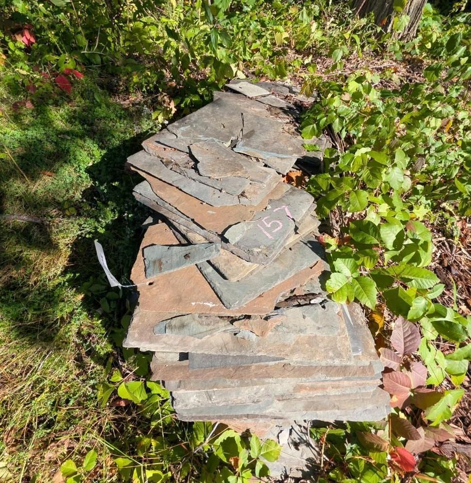 Stack of flat stone slabs in a garden, surrounded by green plants and sunlight