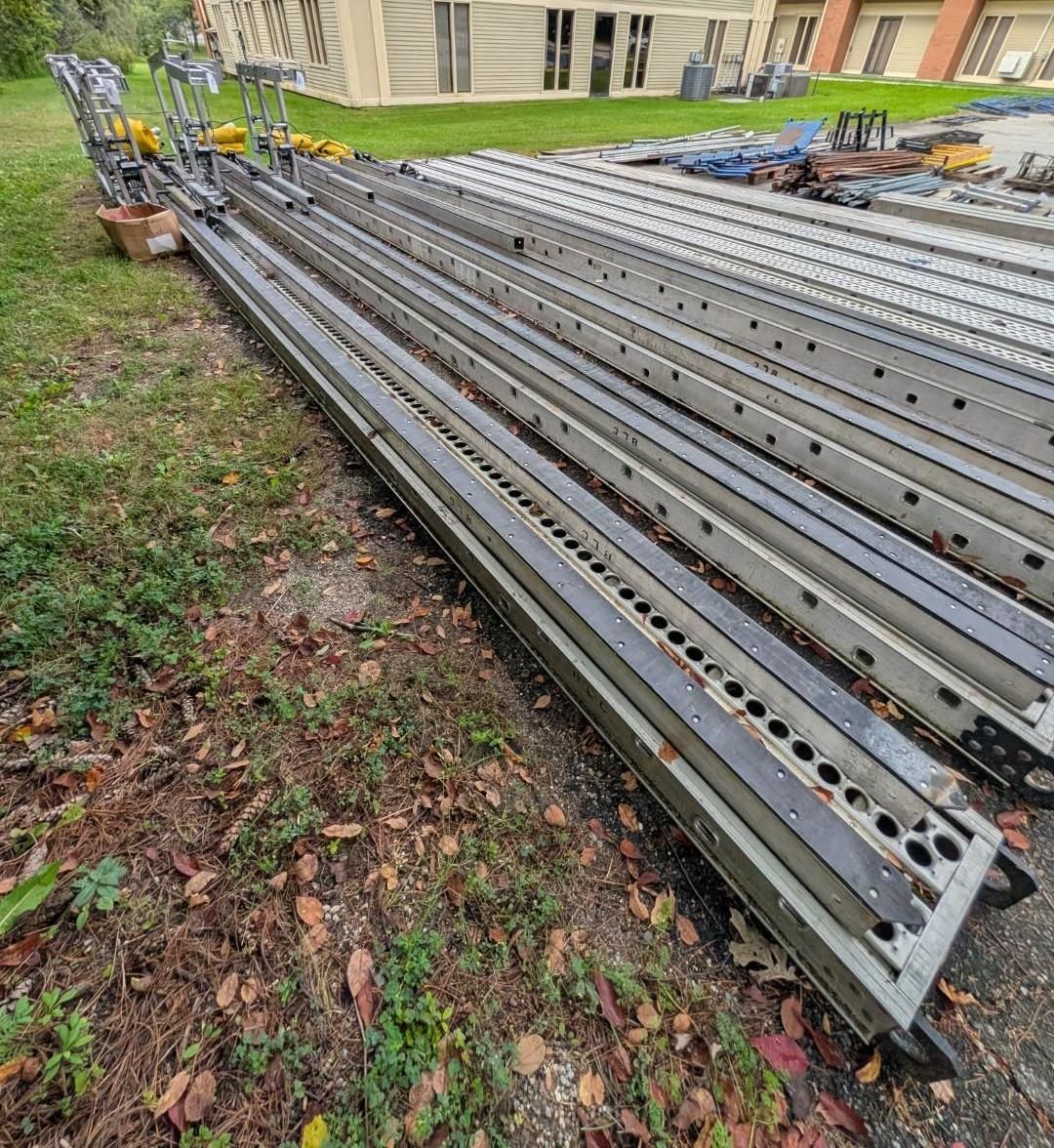 Stacked metal construction beams lying on grass near a building.
