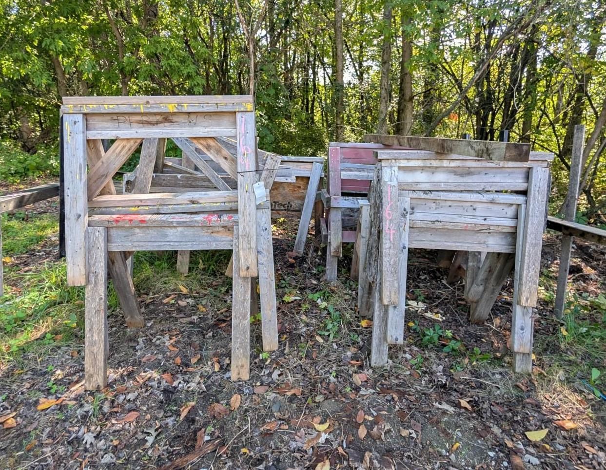 wooden saw horses stacked outdoors in a wooded area.