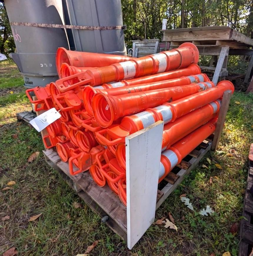 Stack of orange traffic cones and barricade tubes stored on a pallet outdoors.