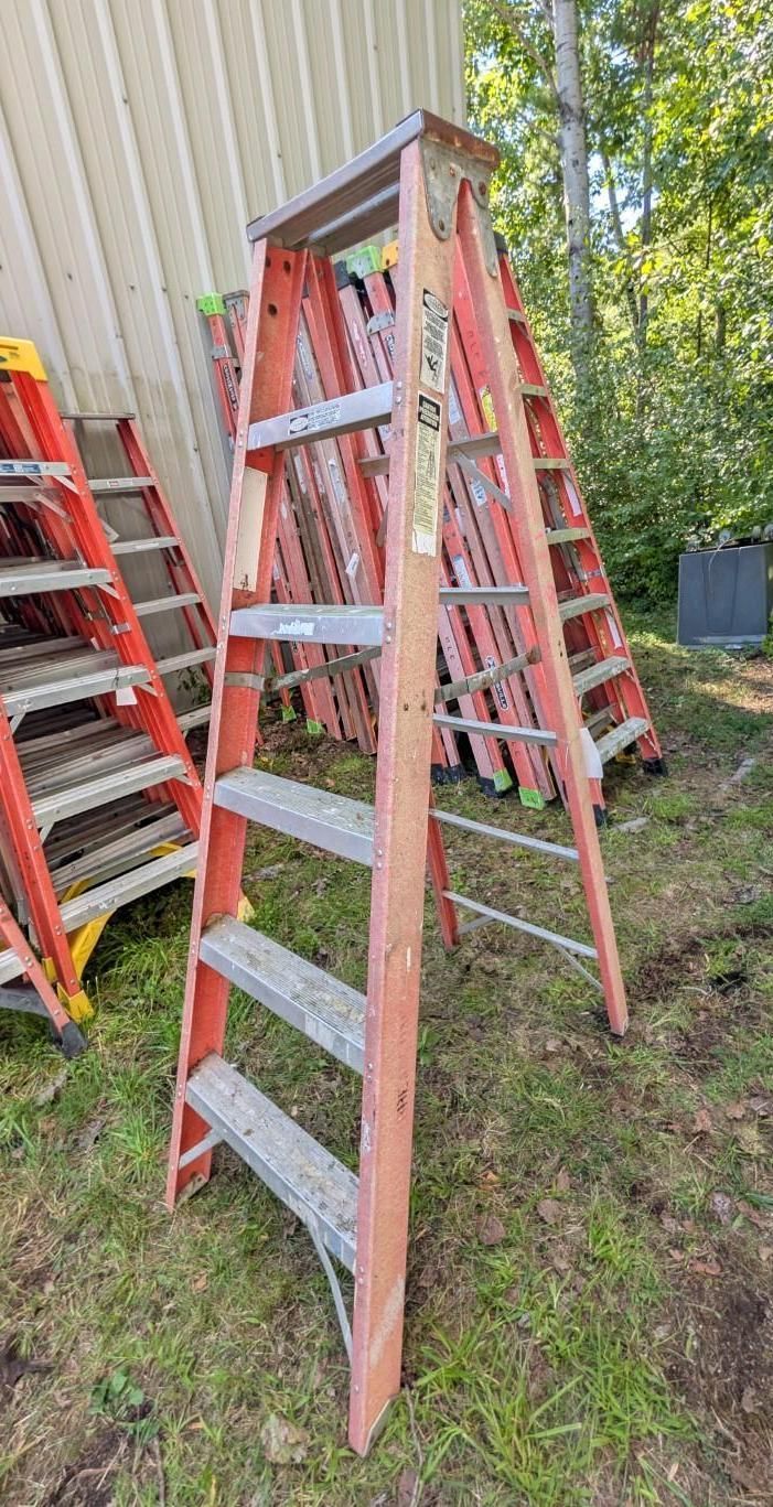 Two-step ladder beside a building, with red ladders and a green yard in the background