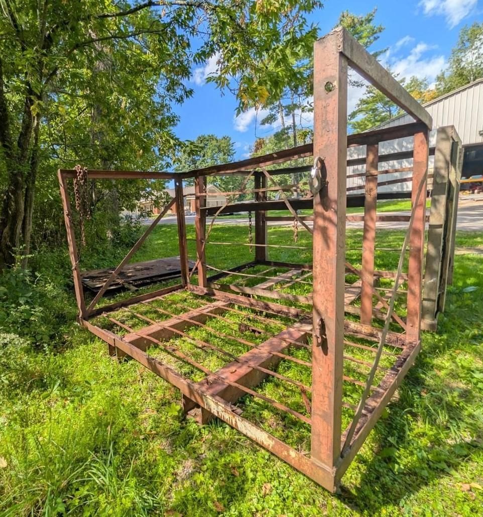 metal cage frame in a grassy yard beside a building, with trees and blue sky.