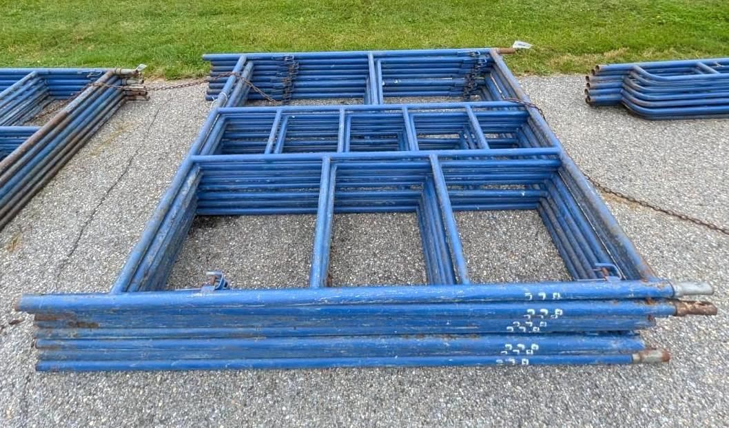 Blue metal scaffolding frames and panels stacked on a gravel lot outdoors