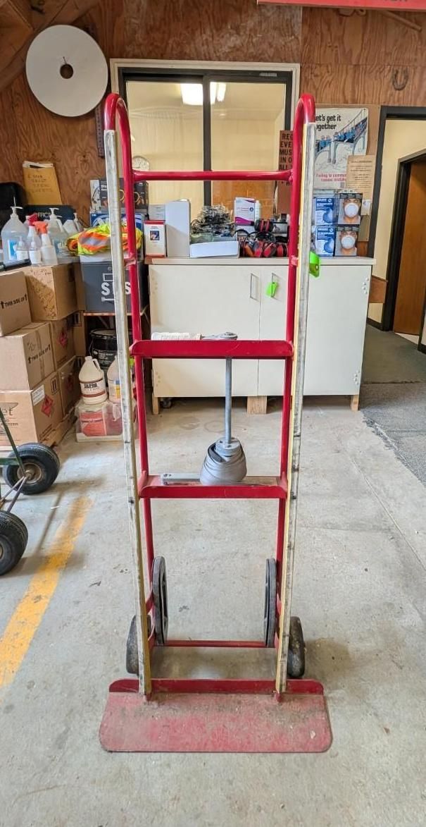 Red metal hand truck with a white panel, standing in a workshop garage.