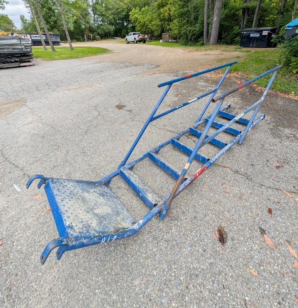 Blue metal staircase and ramp frame lying on gravel in a parking lot.