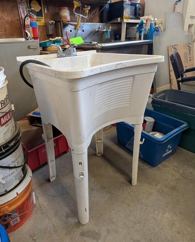 White utility sink on four legs in a workshop or garage, with bins and tools nearby