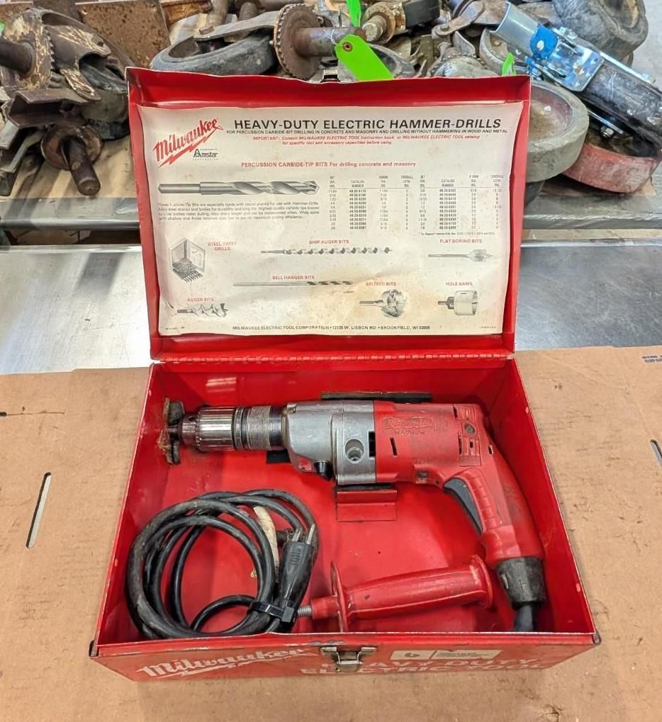 Red Milwaukee drill kit in open red case with cord and attachments on a workbench.