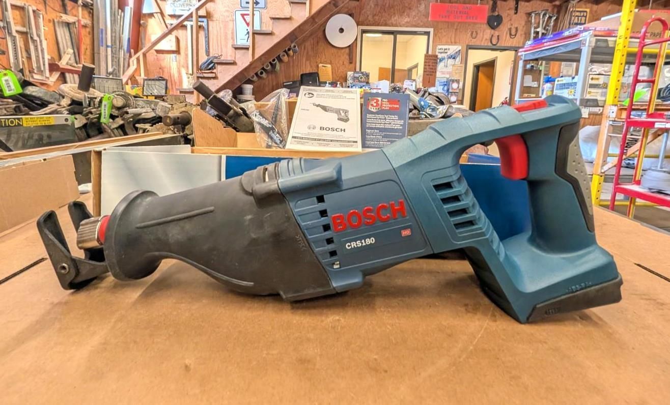Blue Bosch cordless reciprocating saw on a workbench in a workshop, with blade exposed and battery attached