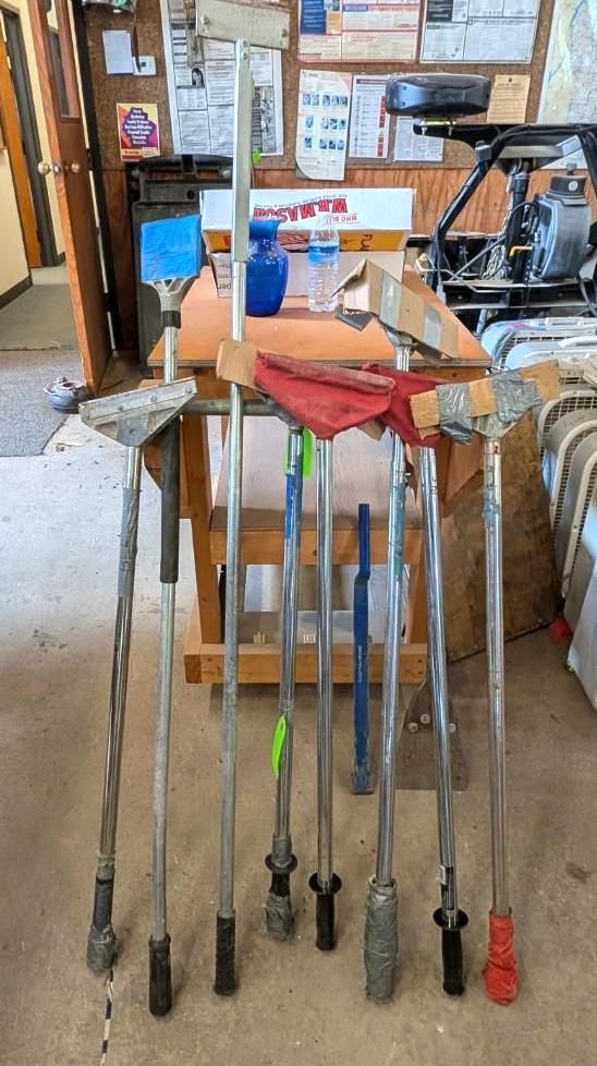A row of golf clubs standing in a garage, with a red bag and tools in the background.