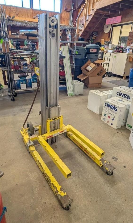 Yellow manual pallet stacker in a warehouse aisle, with forks lowered and wheels on a concrete floor.