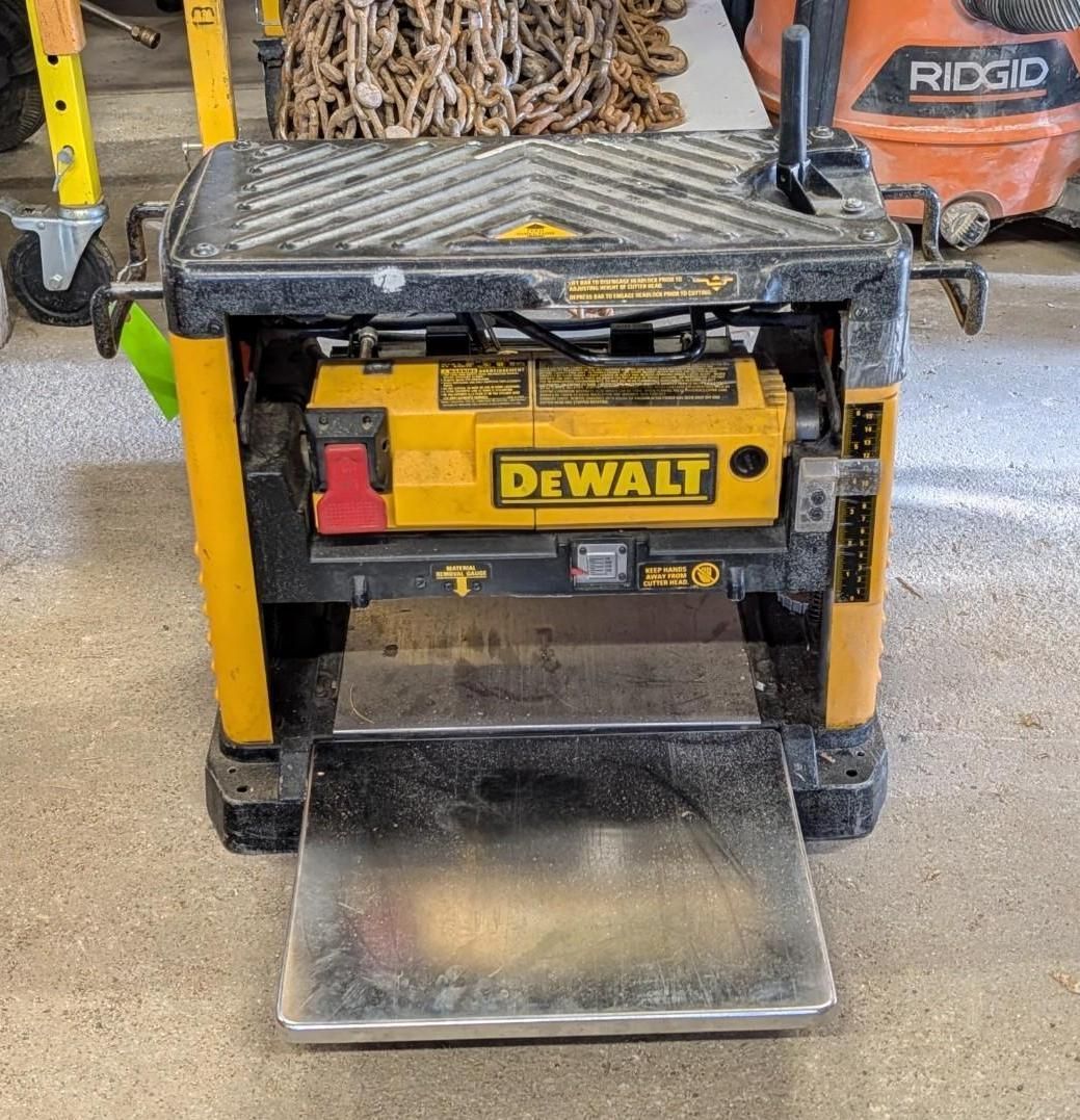 DeWalt portable thickness planer on a workshop floor, yellow and black with metal feed tables.