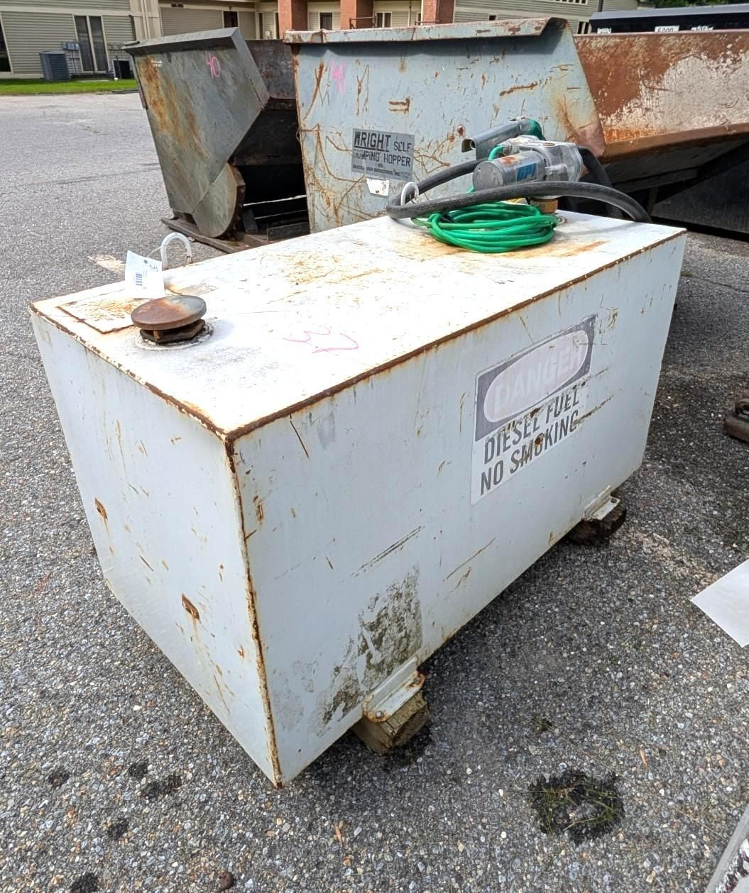 White metal storage tank, hoses on top, sitting outdoors on gravel