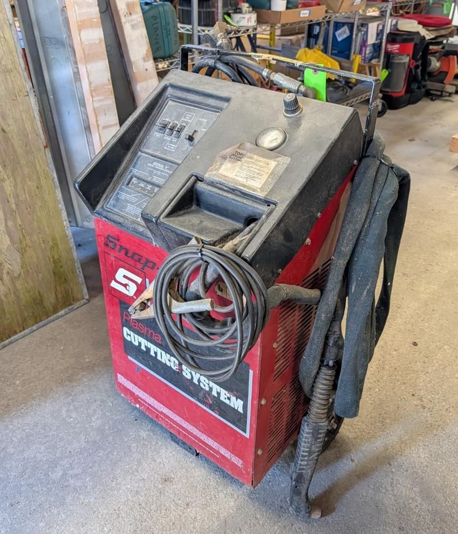 Red automotive machine with cables and hoses in a workshop garage.