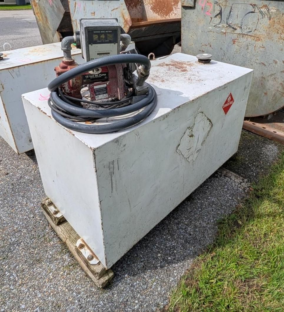 White metal equipment tank with coiled black hose and gauge, sitting on gravel