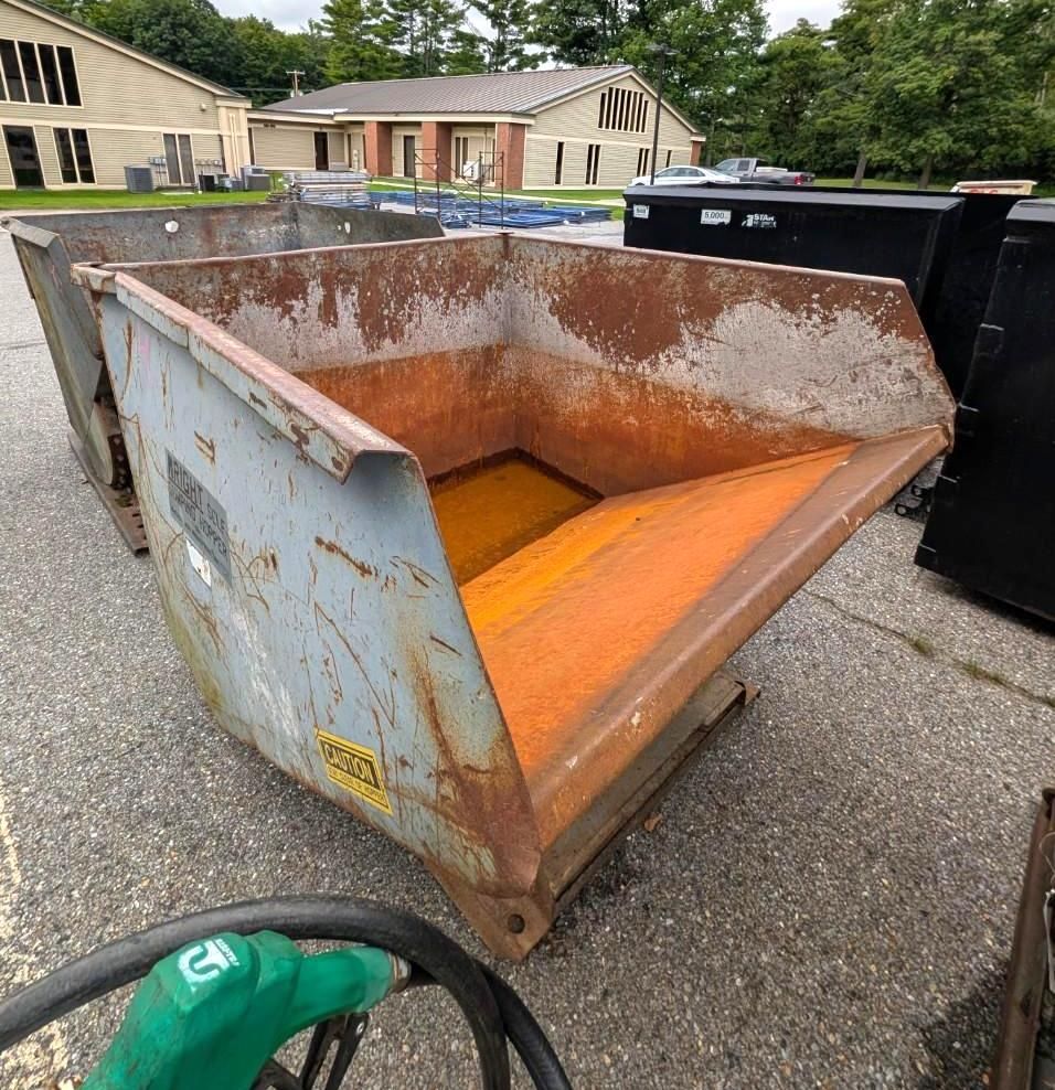 orange construction dumpster in a parking lot near a green hose and black bins.
