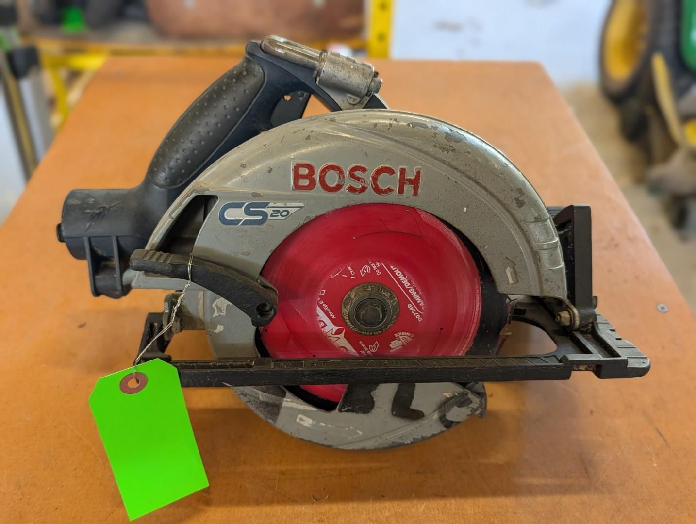 Bosch circular saw with red blade on a wooden workbench, tagged with a bright green label.
