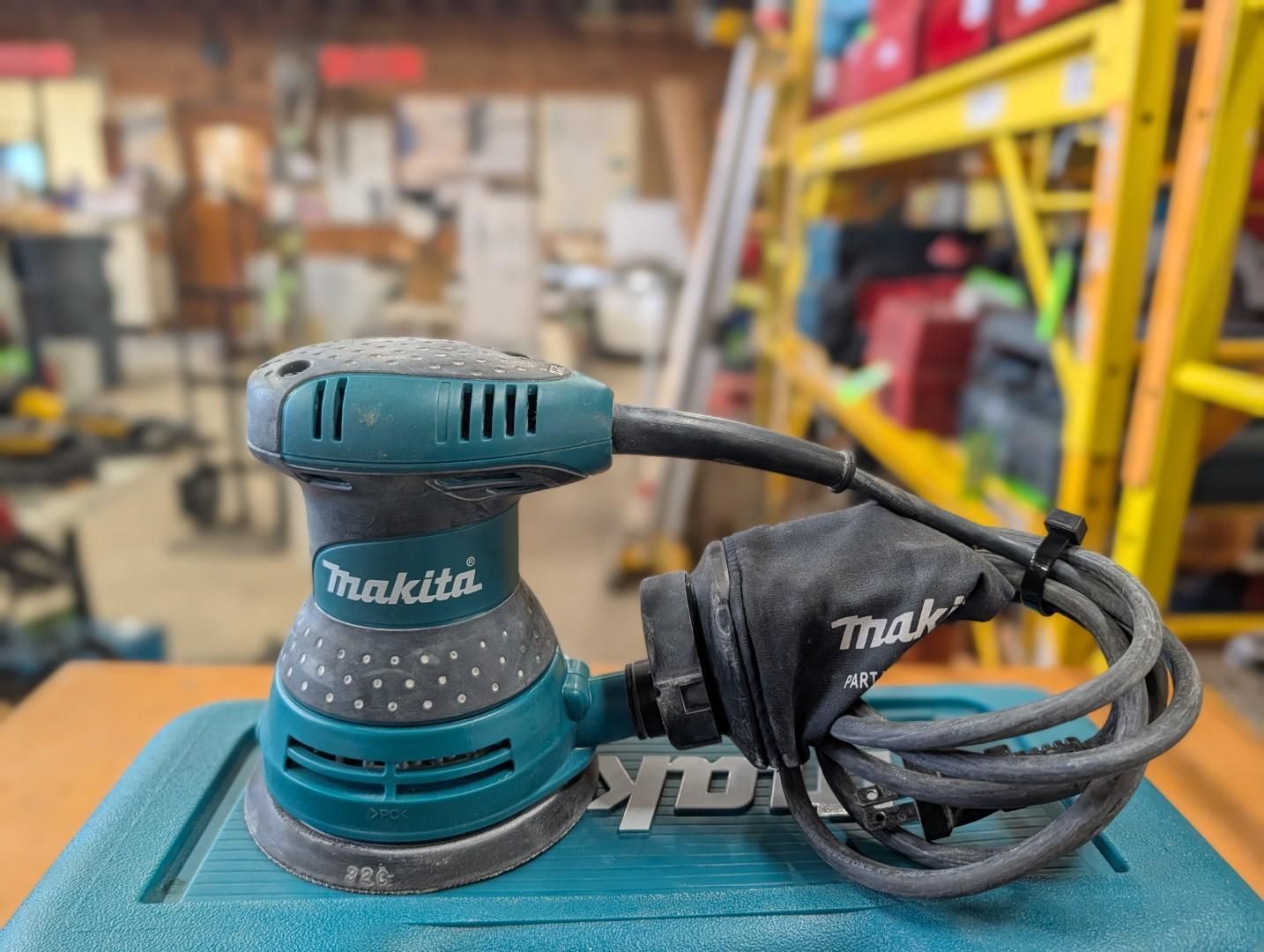 Teal Makita random orbital sander with cord on a workbench in a workshop