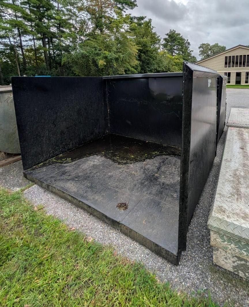 Black metal container or box outdoors on a concrete pad beside grass and a building