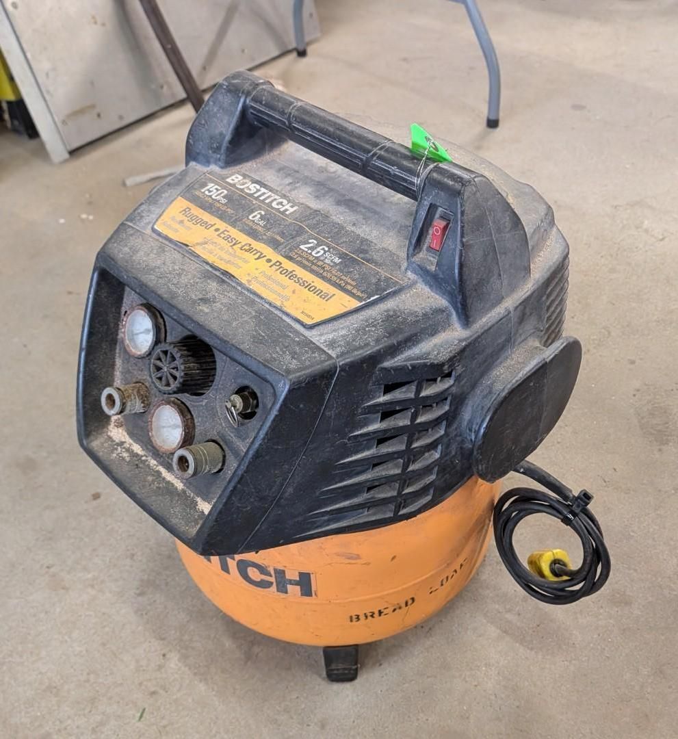 Black air compressor with orange tank and coiled power cord on a concrete floor.