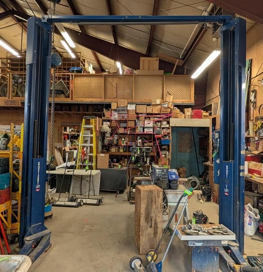 Blue vehicle lift in a workshop with tools, shelves, and equipment.