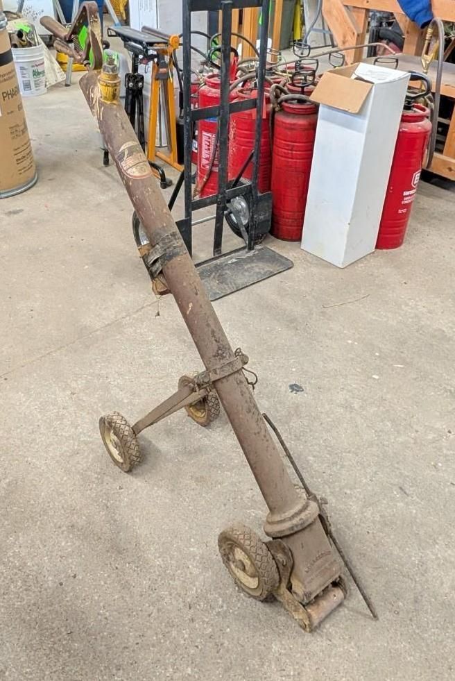 hand truck in a workshop aisle, leaning beside red fire extinguishers and metal racks.