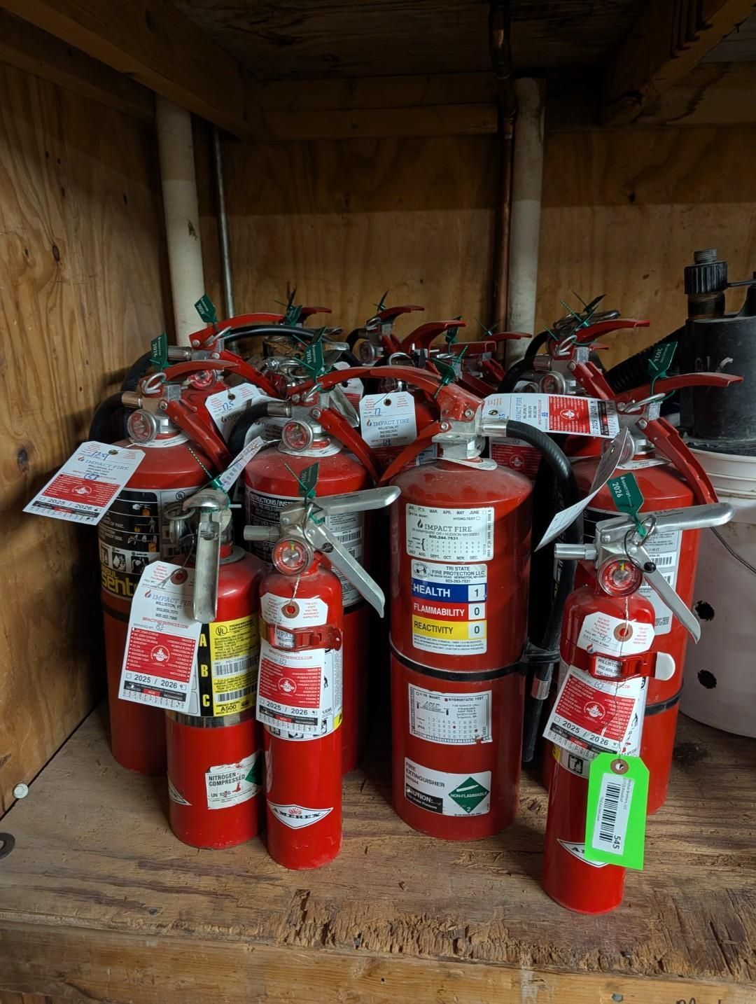 Red fire extinguishers crowded together inside a wooden storage cabinet.