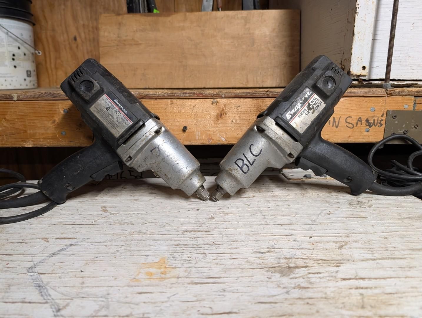 handheld drills crossed on a wooden workbench in a garage-like setting
