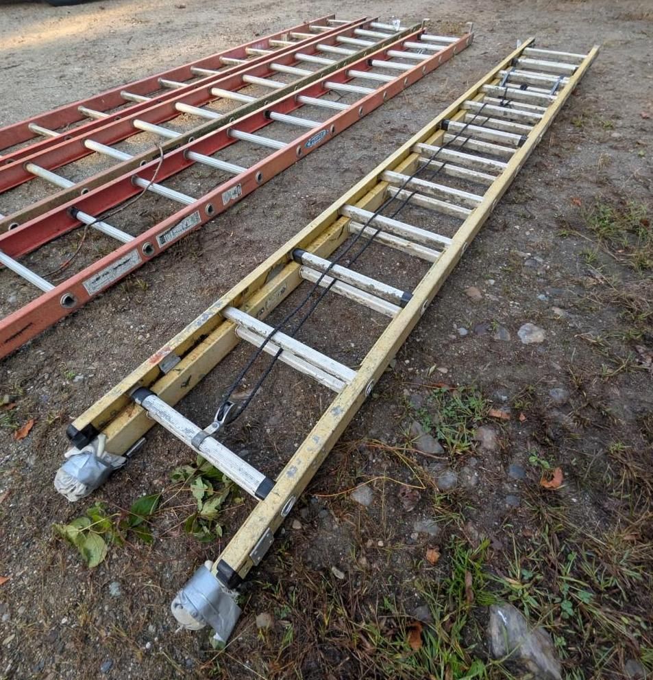 Two ladders lying on gravel, one red and one yellow, with metal wheels at one end