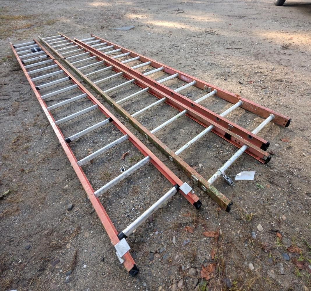 Three red-and-silver extension ladders lying on a gravel surface outdoors