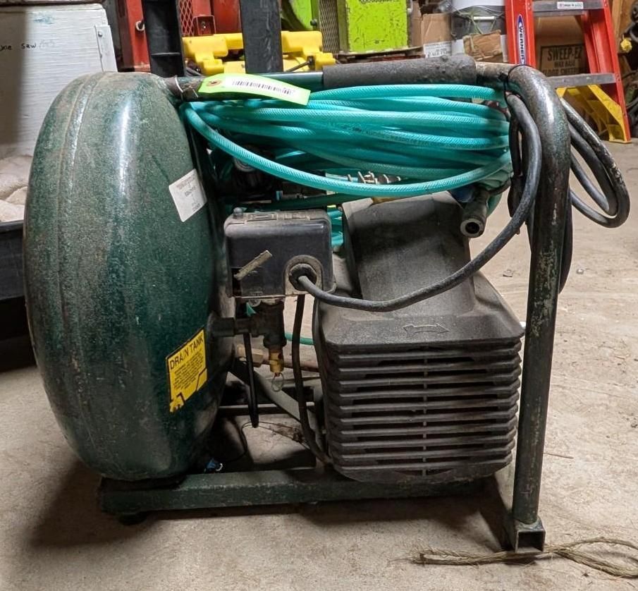 Green air compressor with coiled hoses in a workshop/storage area.