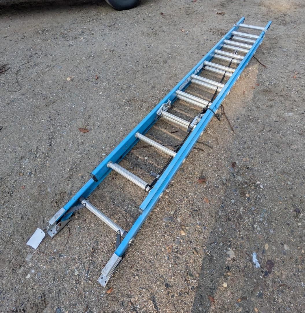 Blue extension ladder lying on gravel ground outdoors