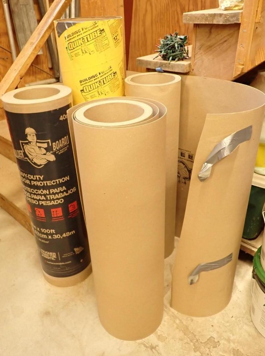 Three rolled mats, black and tan, stacked in a workshop beside wooden stairs.