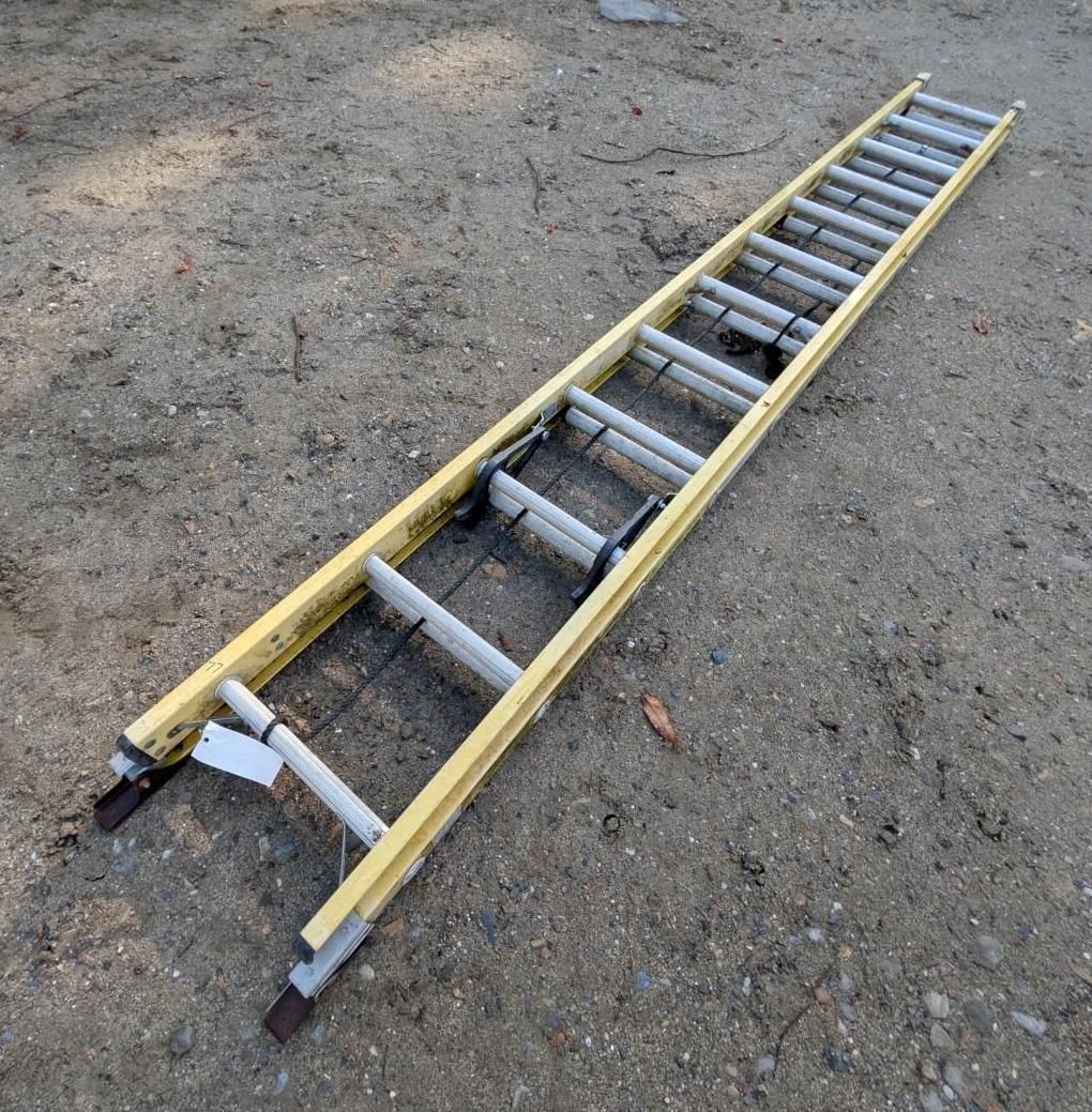 Yellow extension ladder lying on dirt ground, viewed diagonally from above.