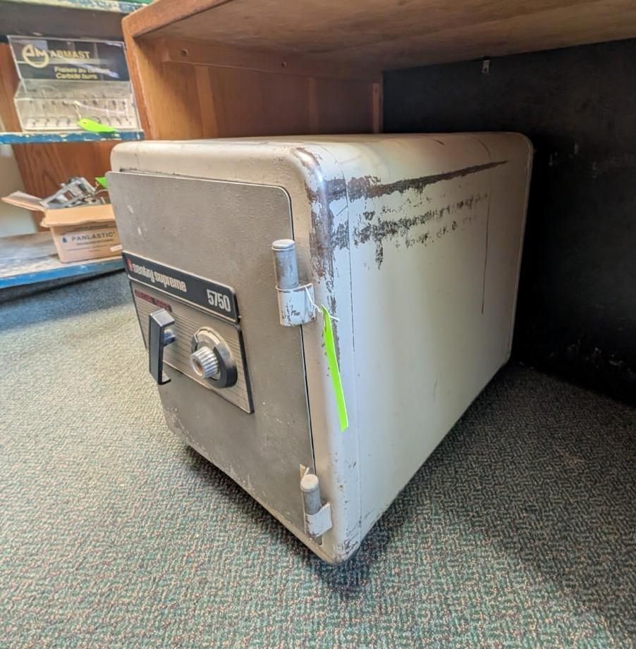 Small gray safe tucked under a wooden desk in a carpeted room