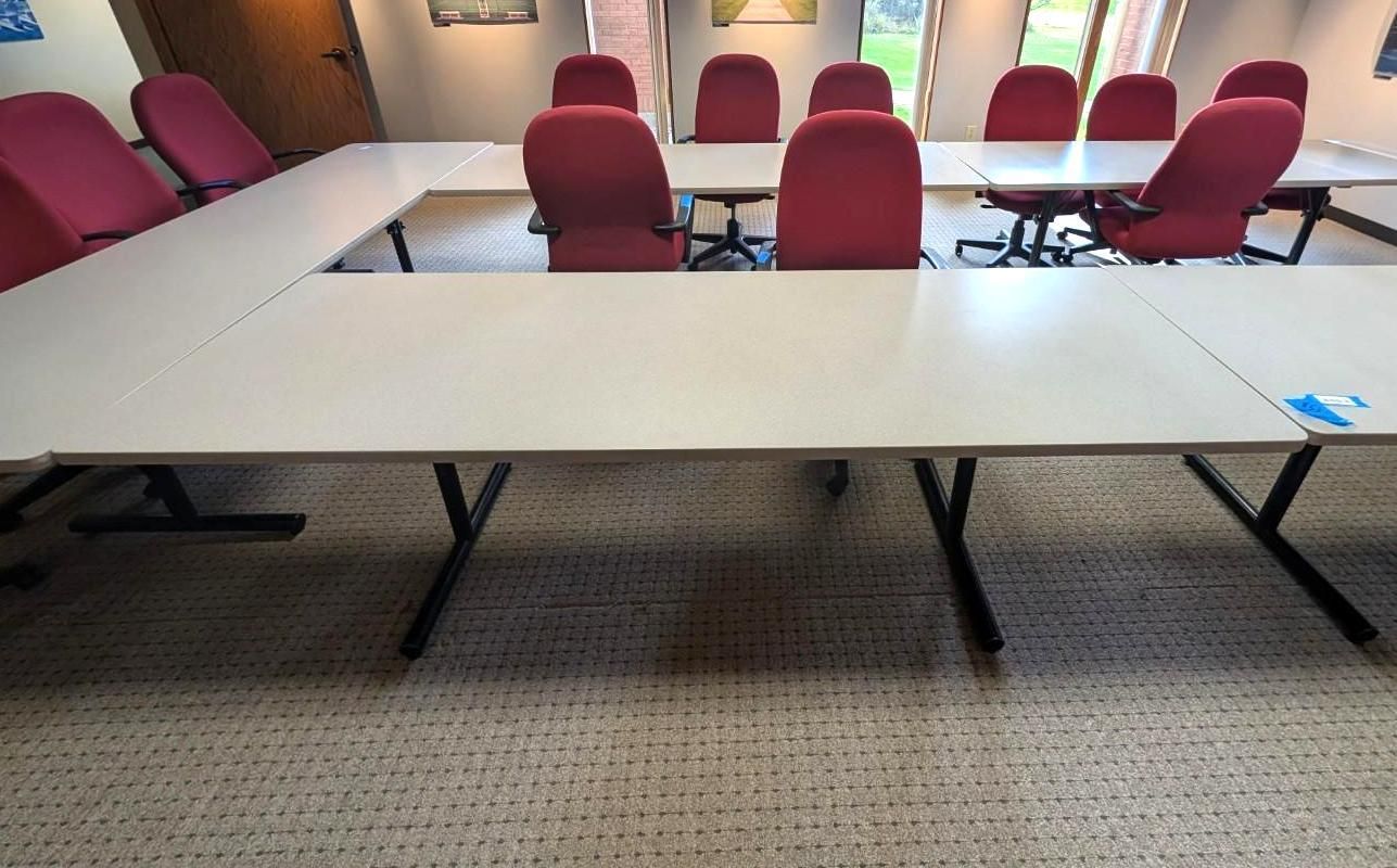 Empty conference room with white tables and red chairs on carpeted floor.