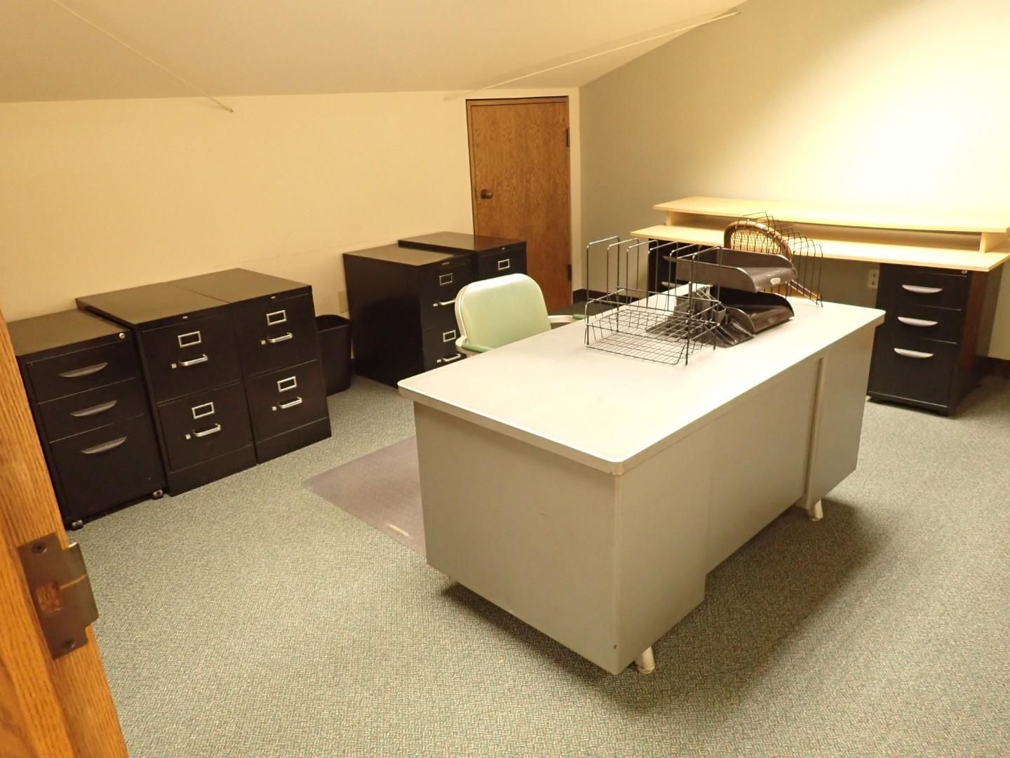 Office with white desk, black filing cabinets, and a wooden door on beige carpet.