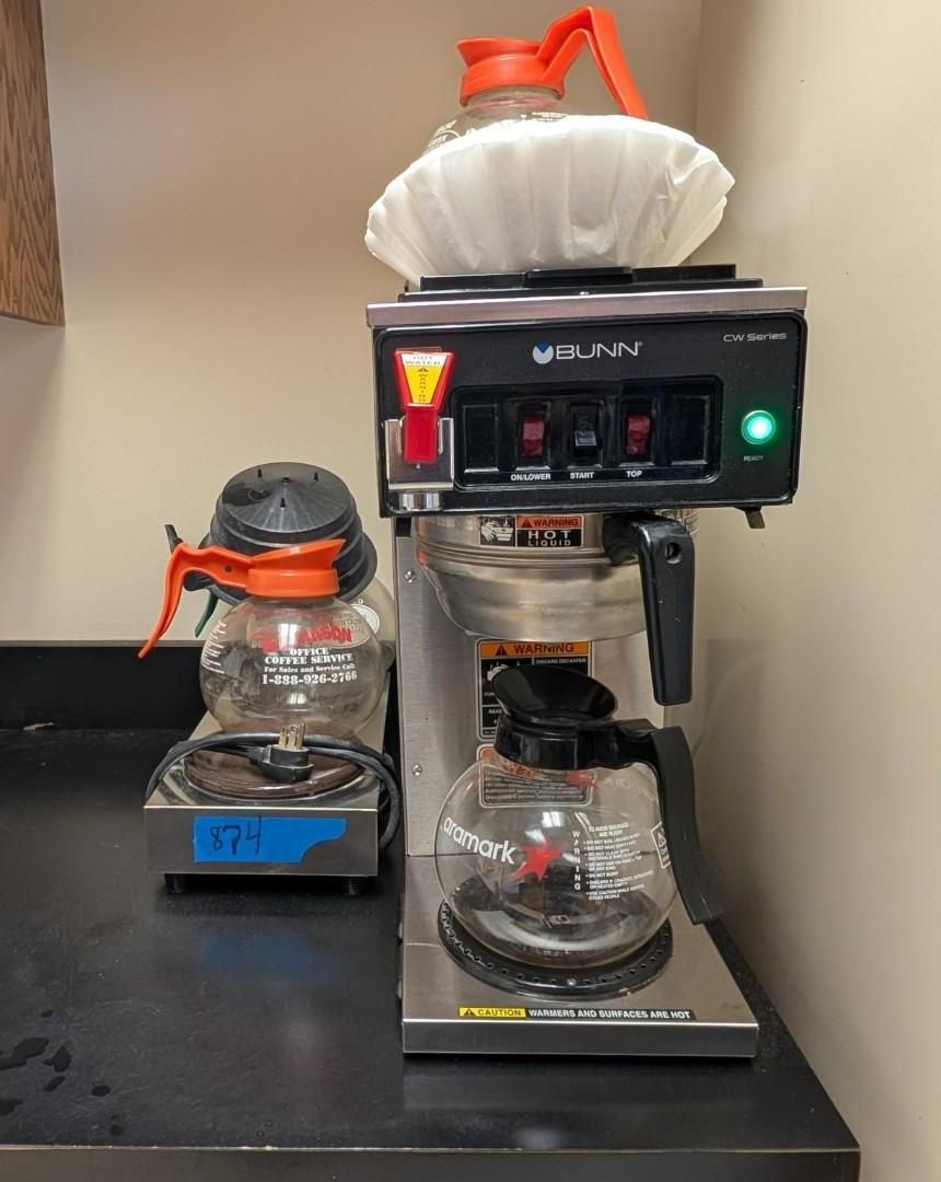 Coffee maker with two glass carafes and a paper filter on a counter; one carafe sits to the left.