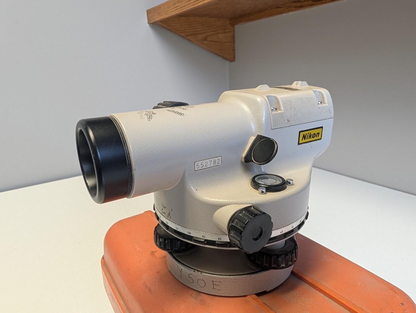 White surveying level instrument on an orange case against a gray wall