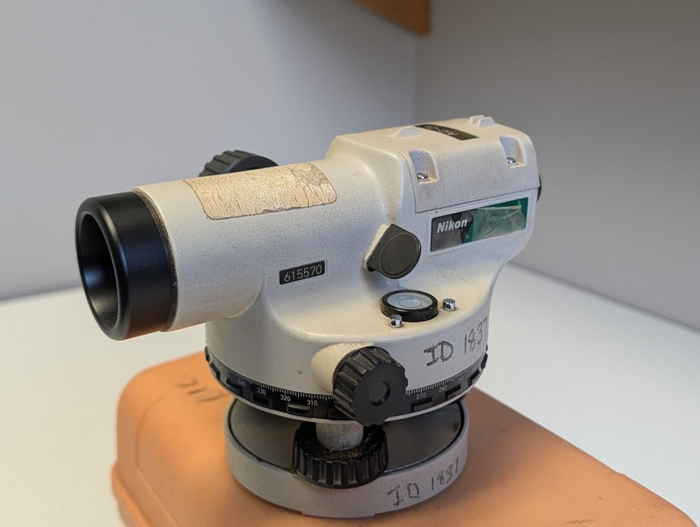 Gray surveyor’s level on a wooden base against a plain background